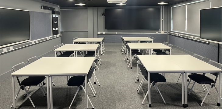 The immersive classroom as an empty classroom with desks, chairs and interactive screens on the walls.