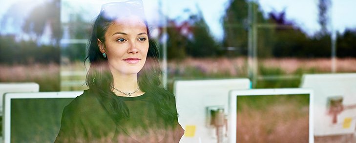 A college worker stands in a computer room with a green landscape reflected in the window.