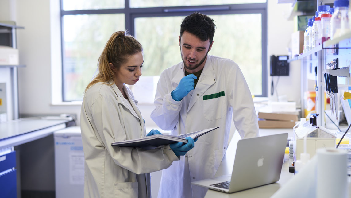 Two medical students work from a laptop and notebook in a hospital laboratory.