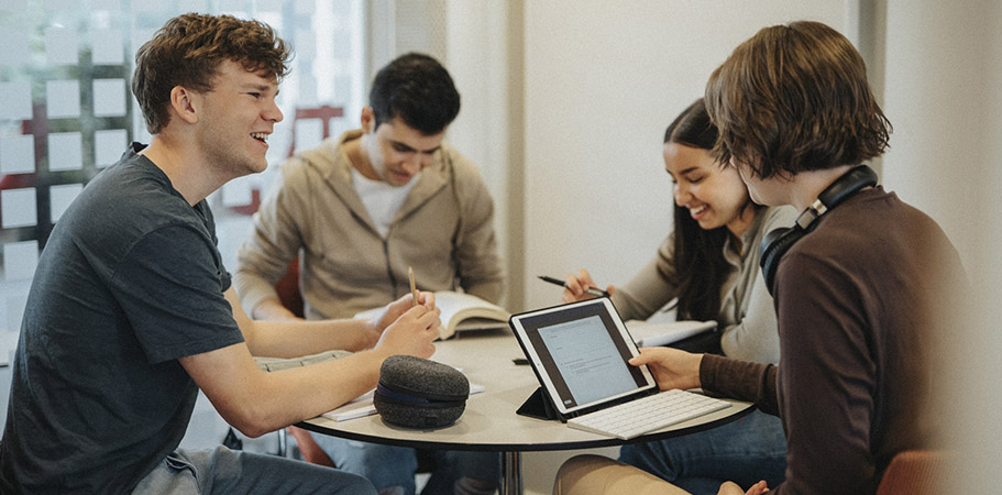 Four students sitting around a table with a tablet.
