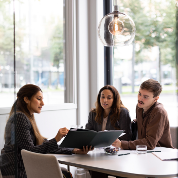 Female real estate agent showing floor plan to young customers while sitting at desk in office