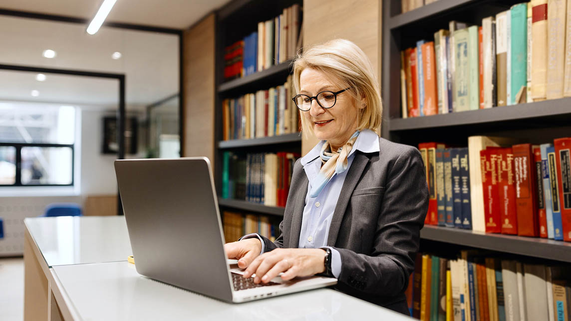 Female staff working on a laptop in a university library.