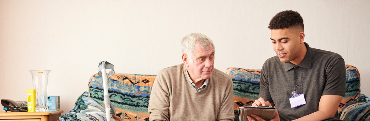 Housing officer sitting with elderly man, using iPad