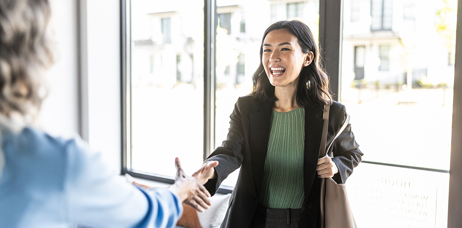 A female graduate smiling and shaking hands with a female colleague.