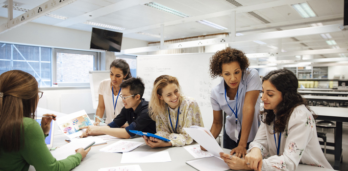 Female students and teachers discuss their work in a classroom.