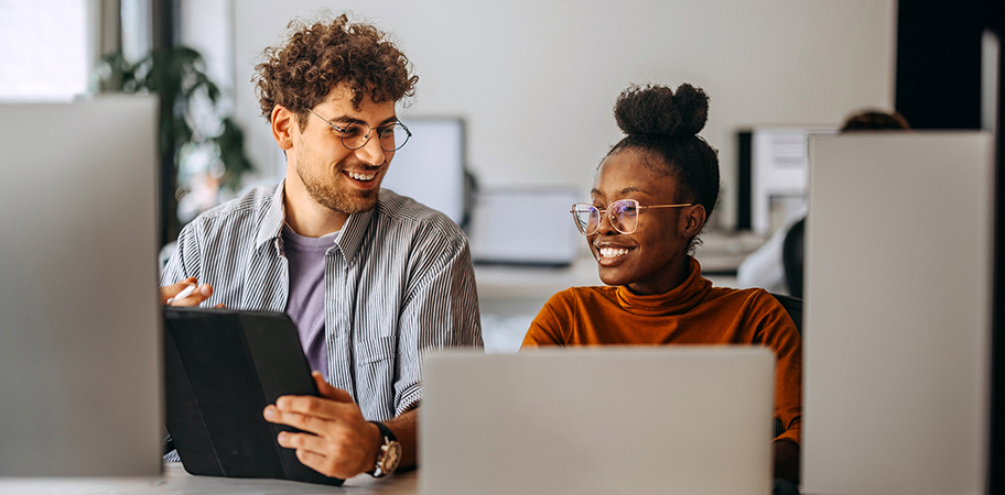 A male and female colleague working at laptops together.