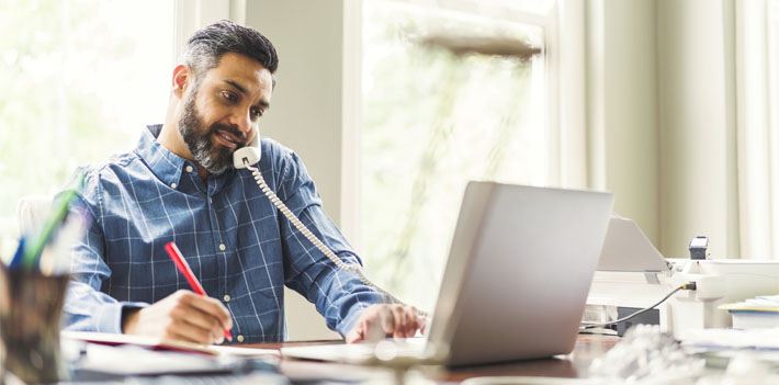 A colleague answers the phone while working on a laptop.
