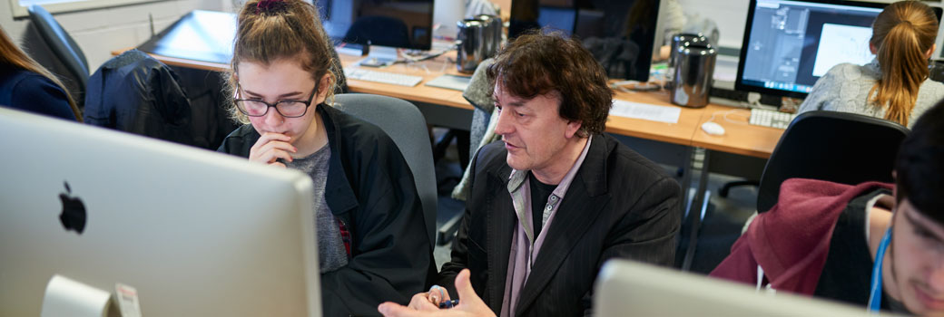 A teacher talks with a student in a computer room.
