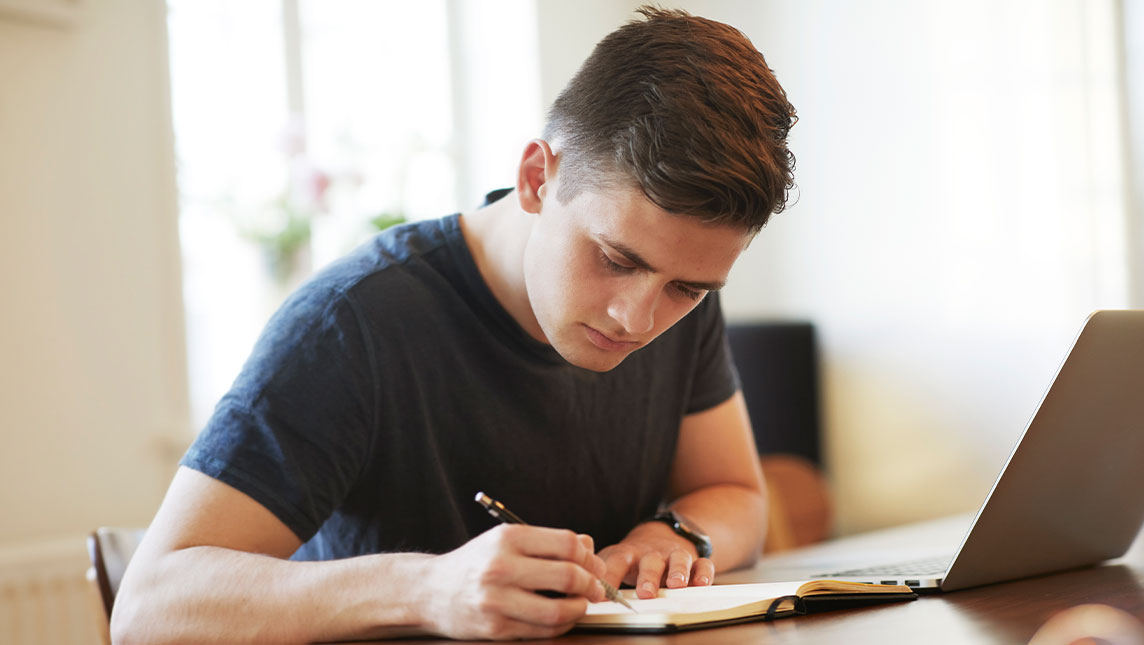 A student makes notes during an online exam.