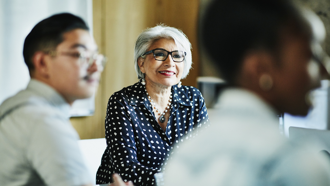 Smiling mature female business owner listening during presentation during meeting in office conference room