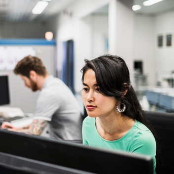 A young woman working on a computer in an office along side her colleagues.