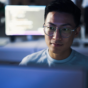 A man wearing glasses looking at a computer screen.